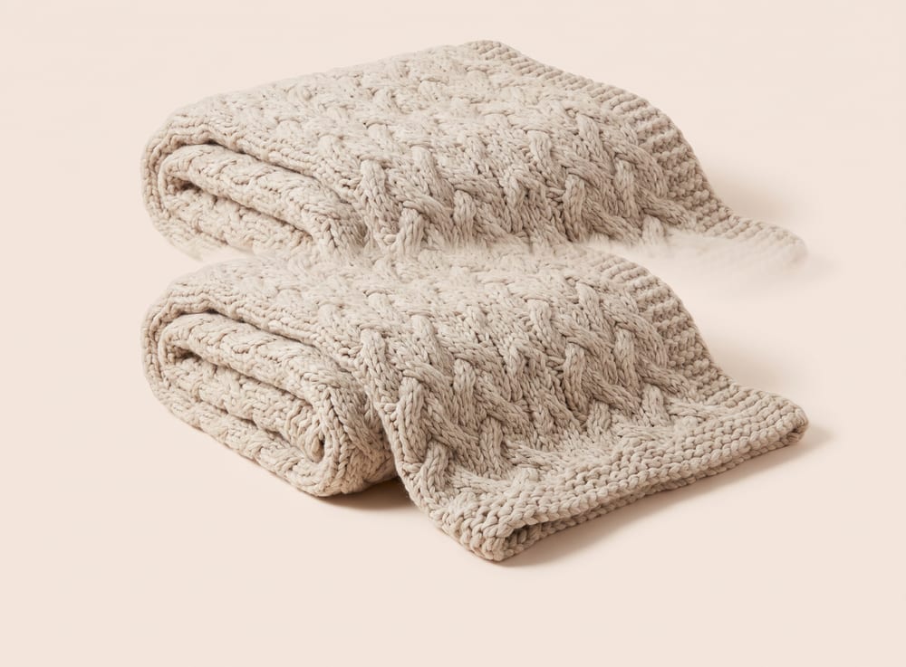 A chunky oatmeal cable-knit throw blanket, loosely folded.