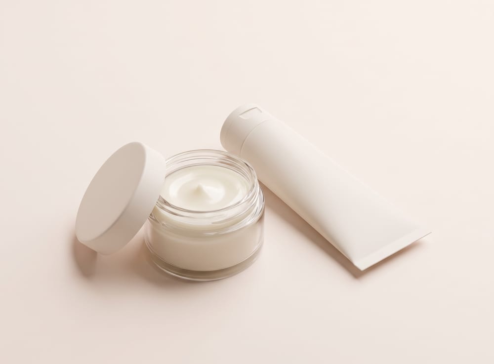 A squat glass jar of pale cream balm with the lid off and a plain tube beside it.