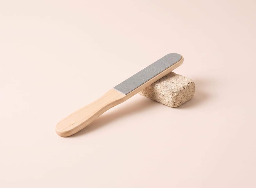 A birch-handled foot file lying beside a small pumice stone.