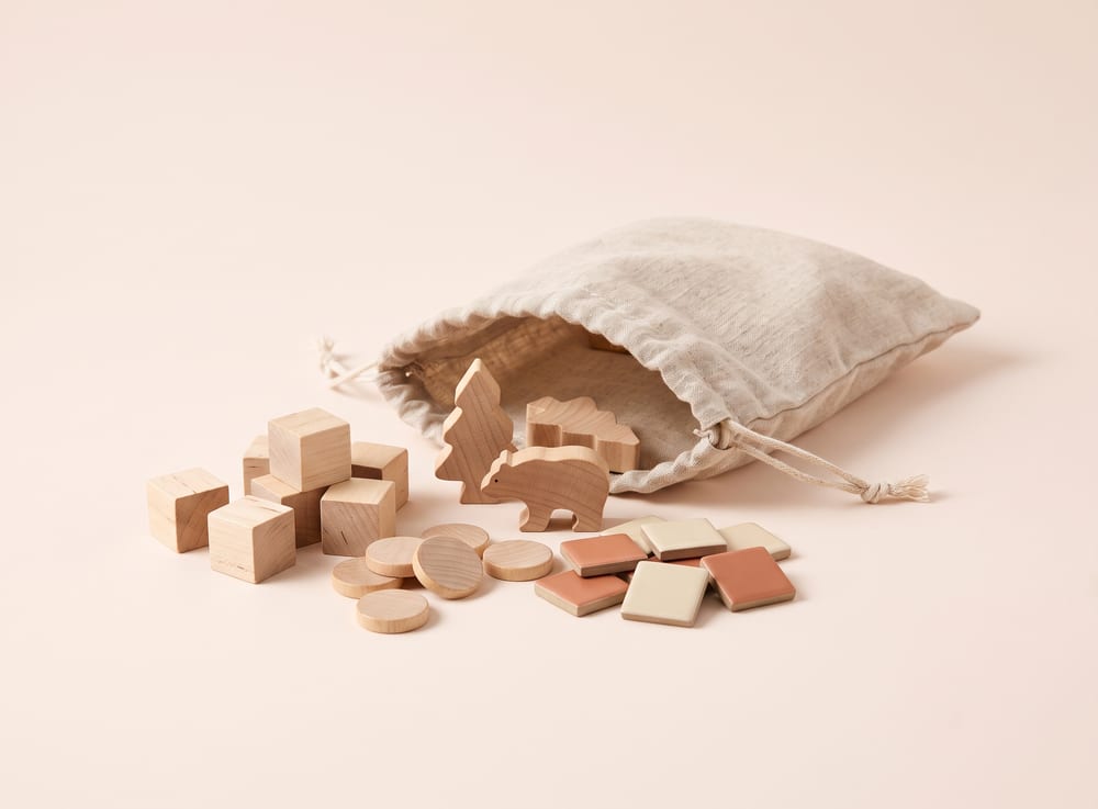 An assortment of wooden board-game pieces, tiles and tokens beside an open linen bag.