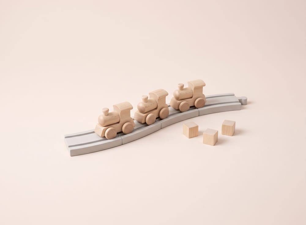 Carved wooden train tokens on pale grey track tiles stepping upward like a staircase.