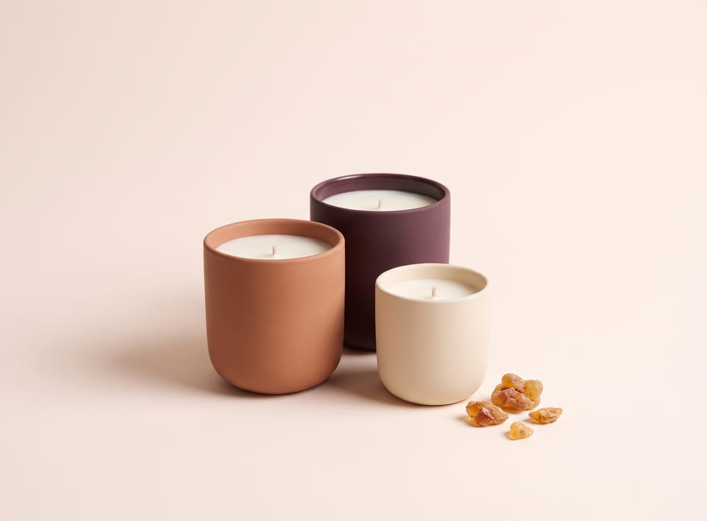 Three unlit candles in clay, plum and cream ceramic vessels with amber resin beside them.
