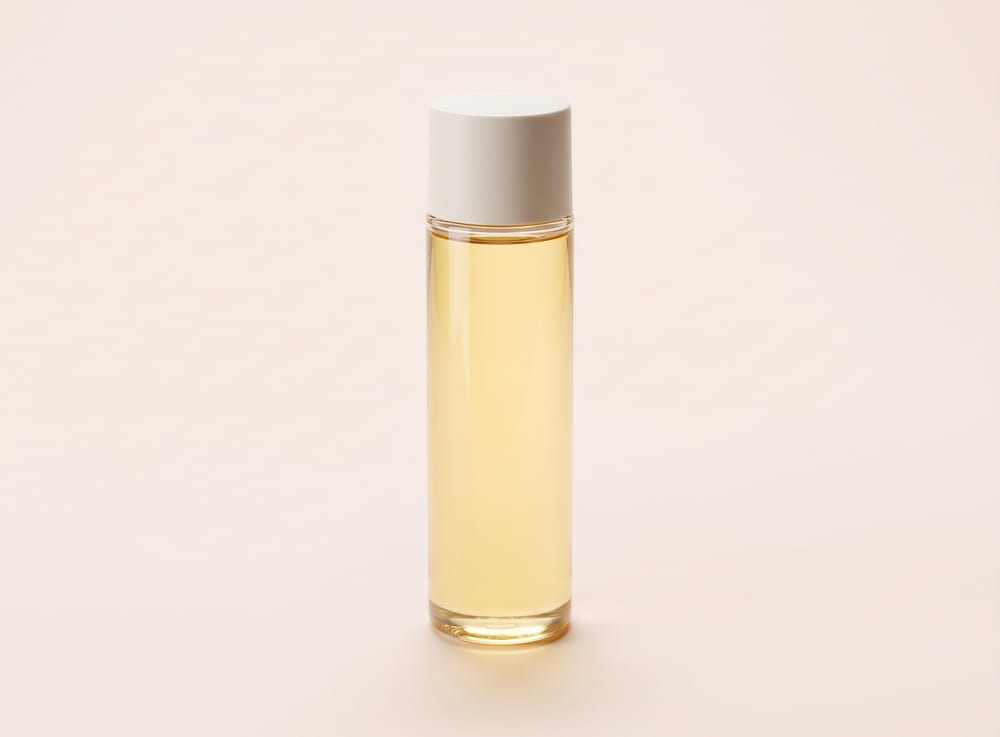 A tall slim glass bottle of pale golden body oil.
