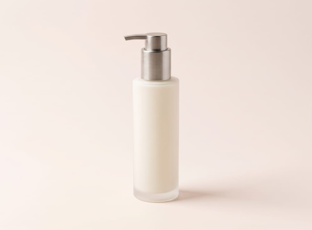 A tall frosted glass pump bottle of pale cream cleanser.